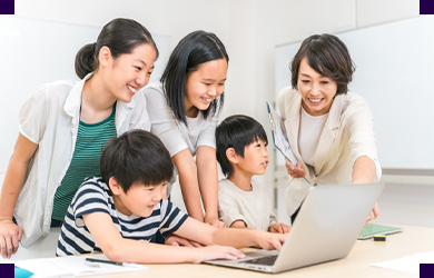 先生と子どもたちがノートパソコンの画面を一緒にのぞき込んでいる様子